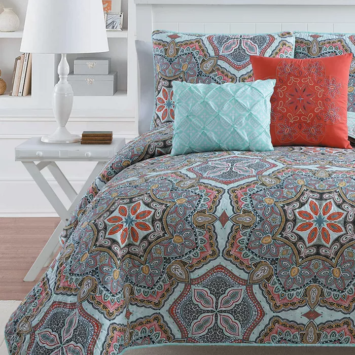A patterned bedspread with coordinated pillows in teal, orange, and brown tones.