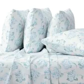 A set of floral-patterned bed linens with light blue flowers includes multiple pillows and a fitted sheet, all displayed on a bed with a gray base.