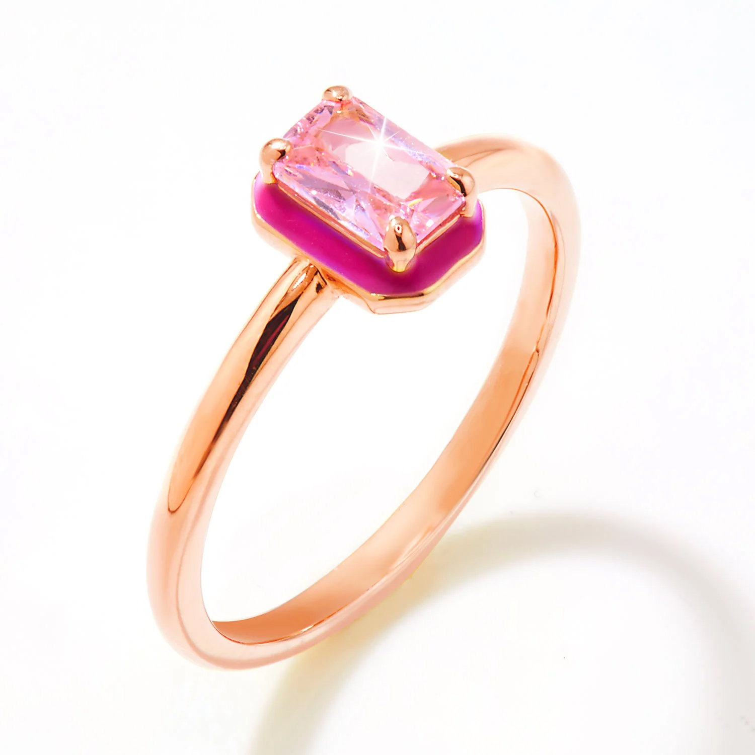 A gold ring featuring a rectangular pink gemstone set on a pink enamel base, with a slim, polished band.