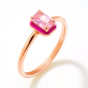 A gold ring featuring a rectangular pink gemstone set on a pink enamel base, with a slim, polished band.