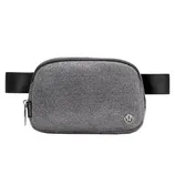 A gray crossbody belt bag with a textured fabric, featuring a zipper closure and an adjustable black strap. It has a small metal logo on the front.