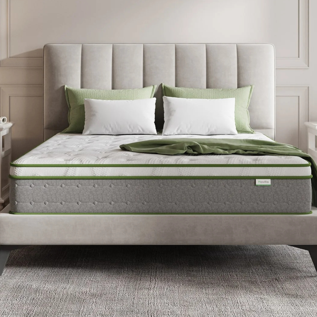 Novilla 10\“ Serenity Mattress features a plush design with a gray base and white top, accented with green trim. It is positioned on a bed with a light gray upholstered headboard, green pillows, and a blanket.