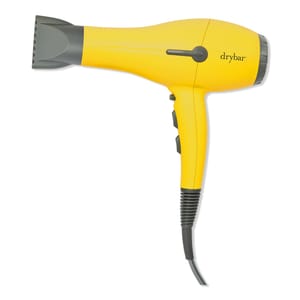 A yellow hair dryer with the \“drybar\“ logo, featuring a concentrator nozzle and two control buttons on the handle.