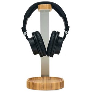 A pair of black over-ear headphones is resting on a sleek headphone stand with a bamboo base and cap.