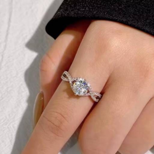 A hand wearing a ring with a large round center stone and a twisted band encrusted with smaller stones, set in a shiny metal.
