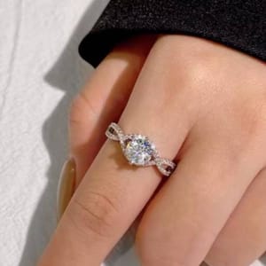 A hand wearing a ring with a large round center stone and a twisted band encrusted with smaller stones, set in a shiny metal.