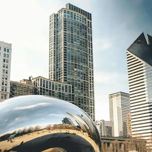 A reflective bean-shaped sculpture, known as Cloud Gate, reflects Chicago's skyline, featuring modern skyscrapers and architectural diversity in an urban setting.