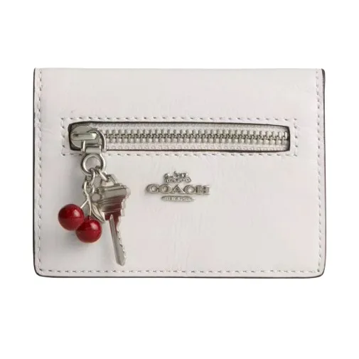 White Coach wallet with a front zipper, silver logo, and a keychain featuring a key and two red cherries.