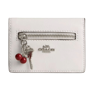 White Coach wallet with a front zipper, silver logo, and a keychain featuring a key and two red cherries.
