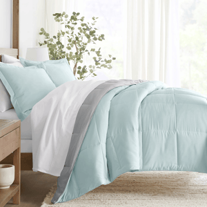 A cozy, light blue and gray comforter set with matching pillowcases, displayed on a neatly made bed with a wooden frame, complemented by soft white curtains and a small plant for a fresh, serene bedroom look.