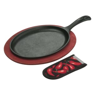 Cast iron sizzle platter with a red wooden trivet and a handle cover featuring red chili pepper designs.