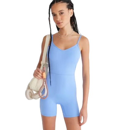 A woman wearing a light blue, fitted one-piece romper with thin straps, holding a white bag with a pink strap over her shoulder.