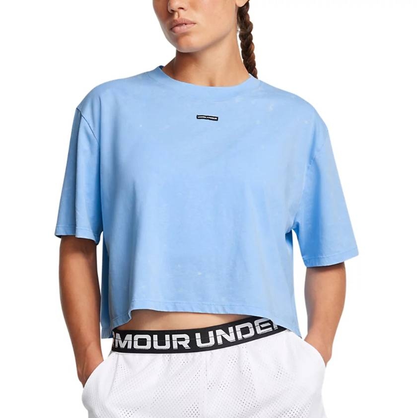 A person is wearing a light blue cropped T-shirt with a small logo on the front, paired with white athletic shorts featuring an \“Under Armour\“ waistband.