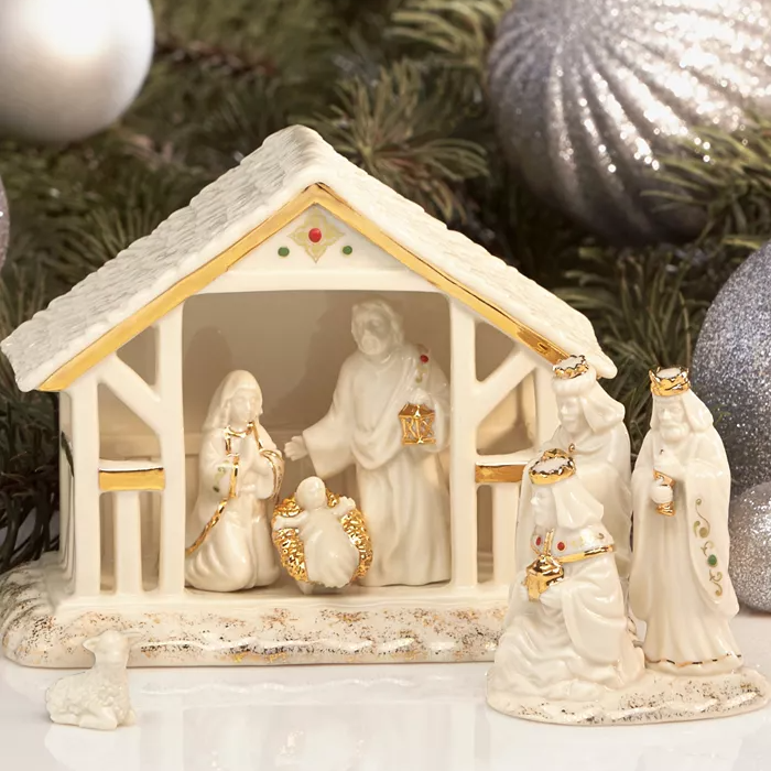 The Lenox Small Nativity Set features intricately crafted porcelain figures with gold accents, including the Holy Family, the Three Wise Men, and a lamb, all housed in a small ivory ceramic stable.