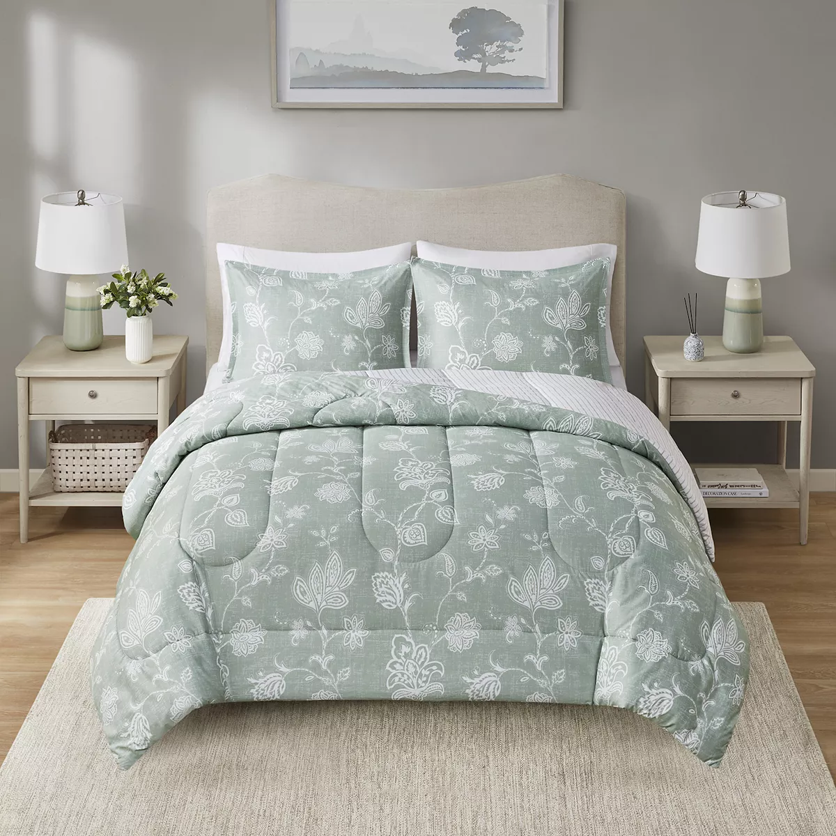 A queen comforter set with a pale green botanical print, including a comforter and two matching pillow shams, displayed on a bed with a neutral headboard and flanked by matching bedside tables with lamps.