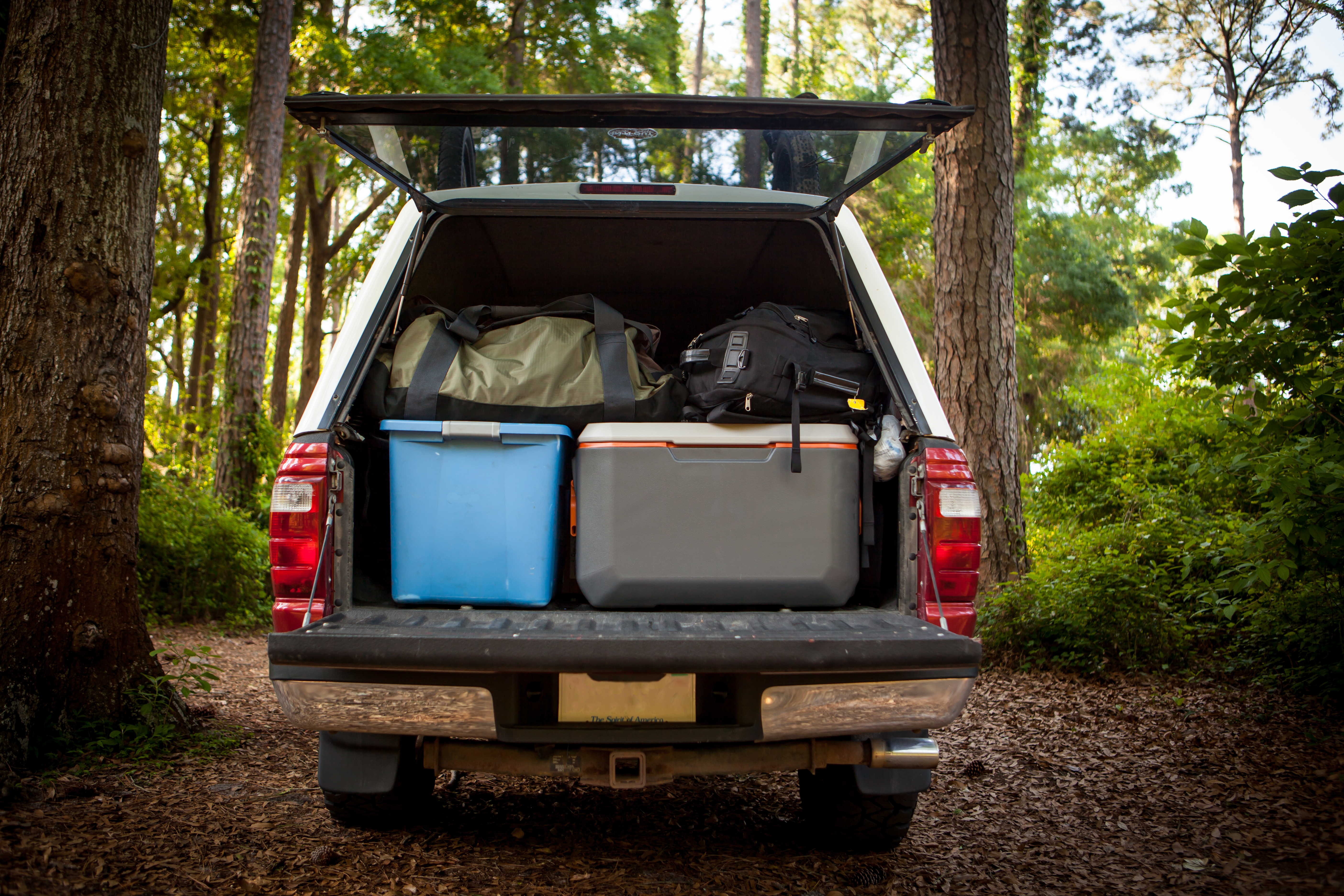 A car trunk open in the woods, filled with bags, coolers, and camping gear.