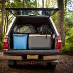 A car trunk open in the woods, filled with bags, coolers, and camping gear.