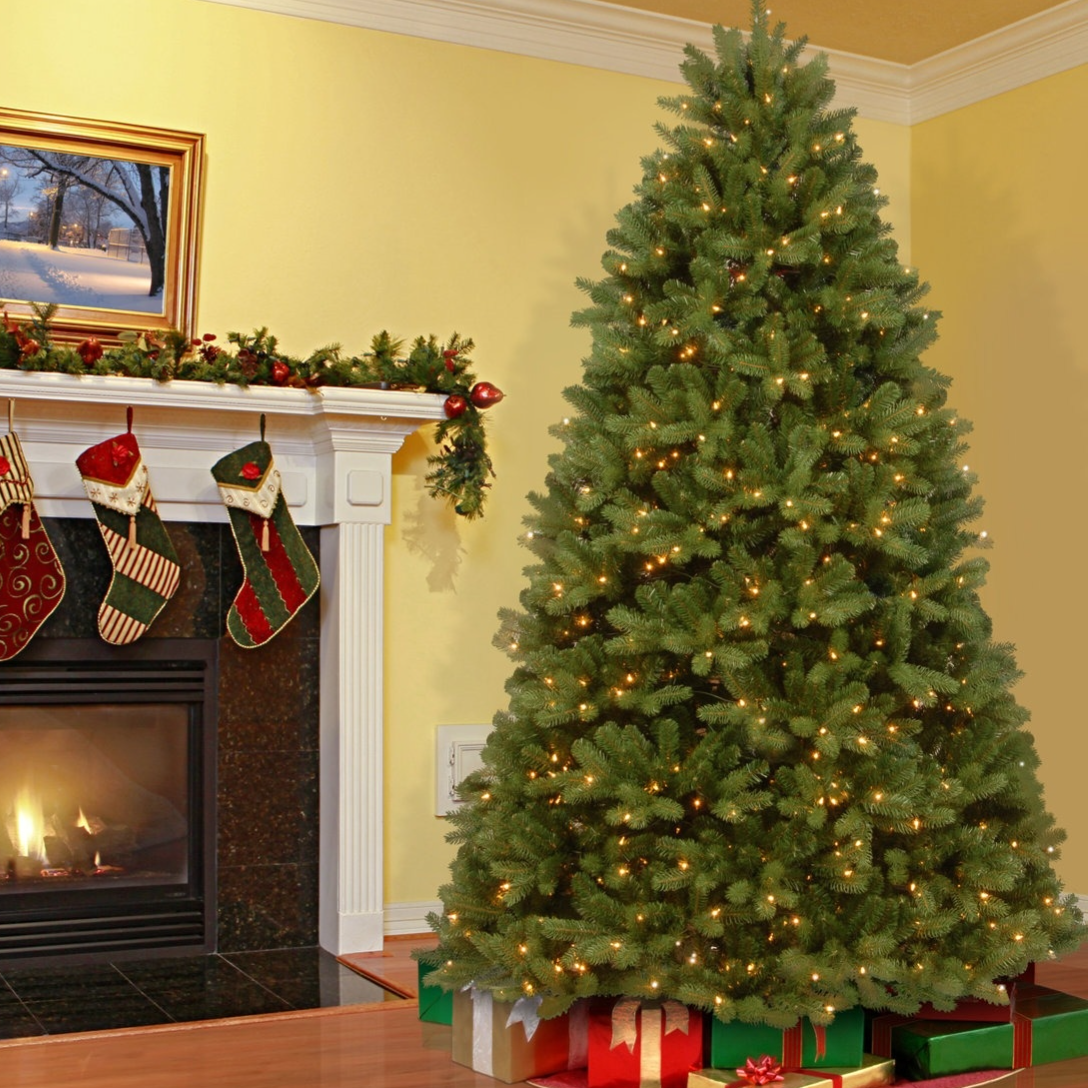 A decorated Christmas tree with lights stands next to a fireplace adorned with garlands and stockings. Wrapped presents are placed under the tree.