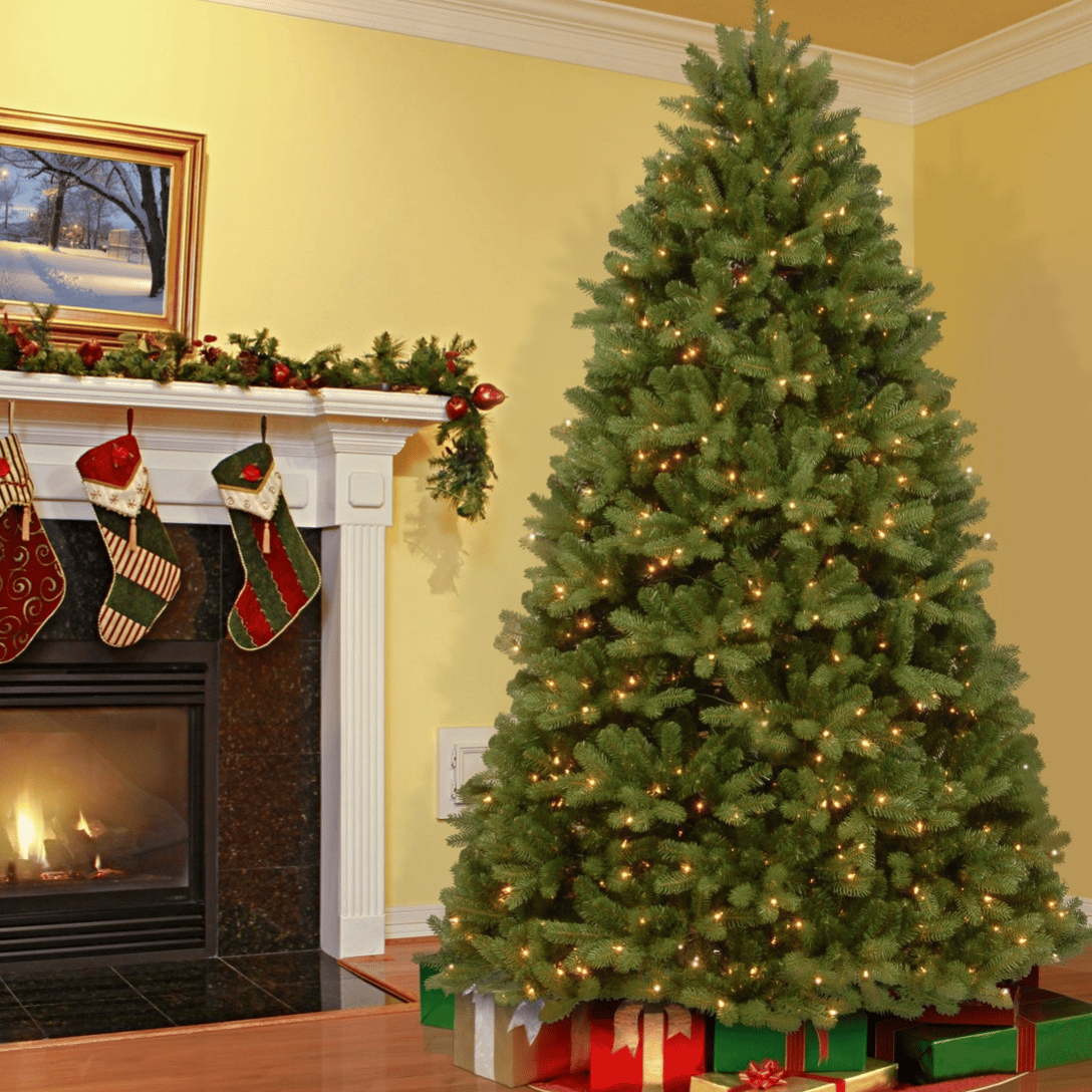 A decorated Christmas tree with lights stands next to a fireplace adorned with garlands and stockings. Wrapped presents are placed under the tree.