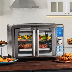 A stainless steel Gourmia air fryer oven with a digital display is shown cooking steaks and vegetables. It features multiple buttons and French doors, positioned on a kitchen countertop with fried chicken and more food around it.