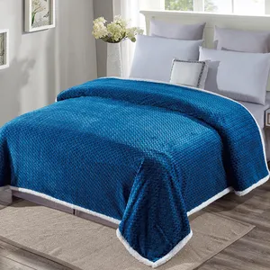 A blue plush blanket with a textured pattern and white trim covers a bed with white pillows in a sunlit bedroom. White flowers in a vase and small framed artworks decorate the room.