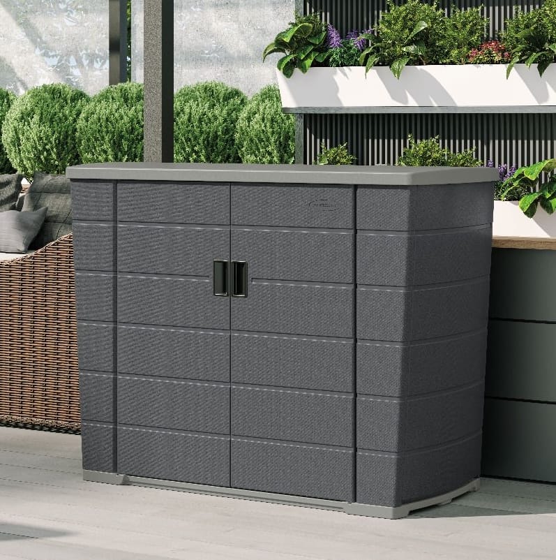 A black outdoor storage cabinet with double doors is placed on a patio, surrounded by plants and outdoor furniture.