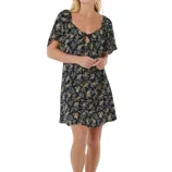 A woman is wearing a black floral mini dress with a front tie detail and short sleeves. She pairs it with black platform sandals.