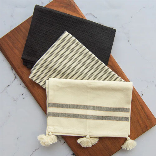 one black and two beige tea towels on a white marble countertop