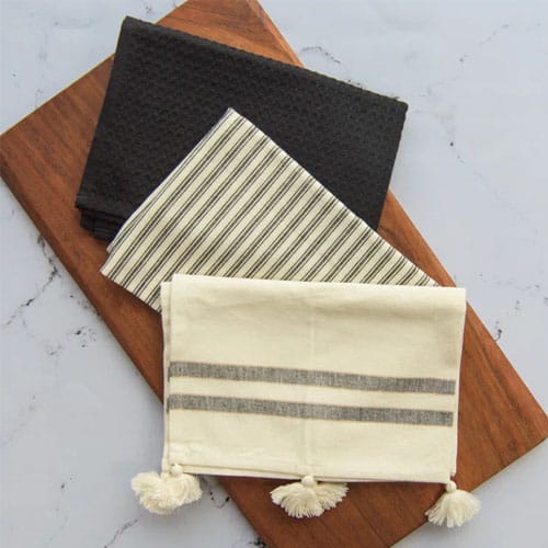 one black and two beige tea towels on a white marble countertop