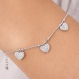 A delicate silver anklet features three heart-shaped charms encrusted with small gemstones, each evenly spaced along a fine chain.