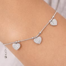 A delicate silver anklet features three heart-shaped charms encrusted with small gemstones, each evenly spaced along a fine chain.