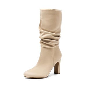 A pair of mid-calf women's boots in a beige color with a slouchy shaft and a chunky high heel.