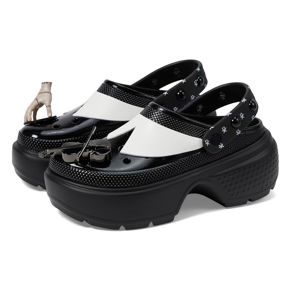 Black and white platform clogs featuring a punk, gothic design with embellishments, including a violin and a hand charm, inspired by Wednesday Addams. The straps and toe areas have distinct skull and cross motifs.