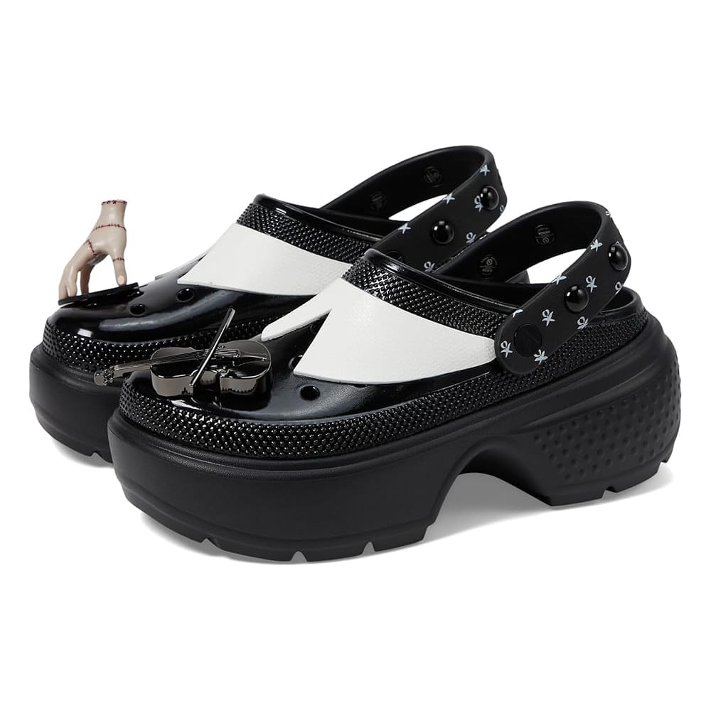 Black and white platform clogs featuring a punk, gothic design with embellishments, including a violin and a hand charm, inspired by Wednesday Addams. The straps and toe areas have distinct skull and cross motifs.