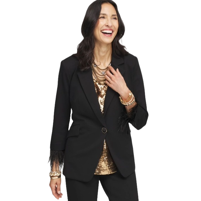 A smiling woman is wearing a black blazer with feather trim on the sleeves, paired with a gold sequin top. She's accessorized with layered necklaces and bracelets.