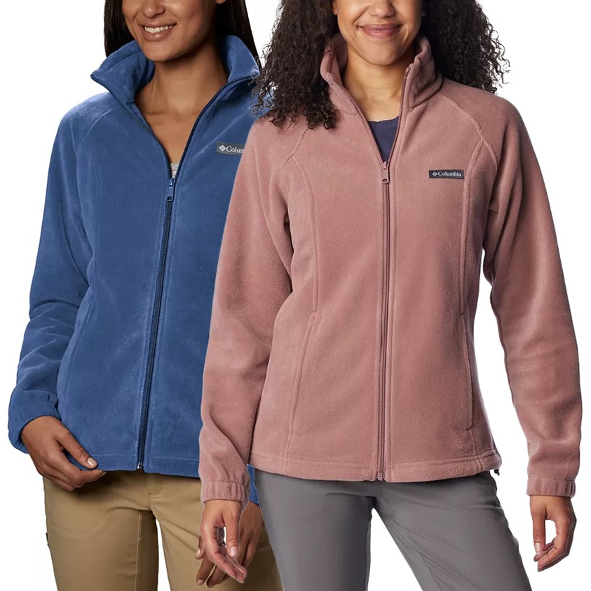 Two women are wearing Columbia Women's Benton Springs Fleece Jackets, one in blue and the other in pink, with the Columbia logo on the chest. The jackets have full zips and stand-up collars.