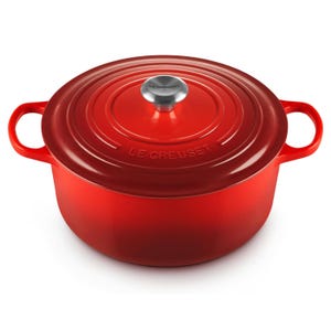 A red Le Creuset enameled cast iron Dutch oven with a metal knob and handles.