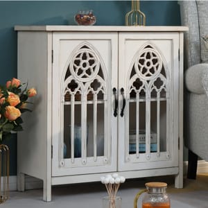 A white wooden sideboard with gothic-arch glass doors, accompanied by decorative items including a vase of roses and a gold-toned bottle.