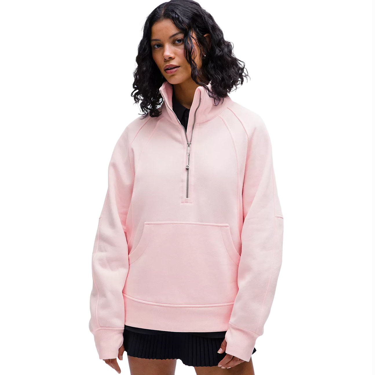 A person wears a light pink, oversized half-zip sweatshirt with a front pocket and black skirt.