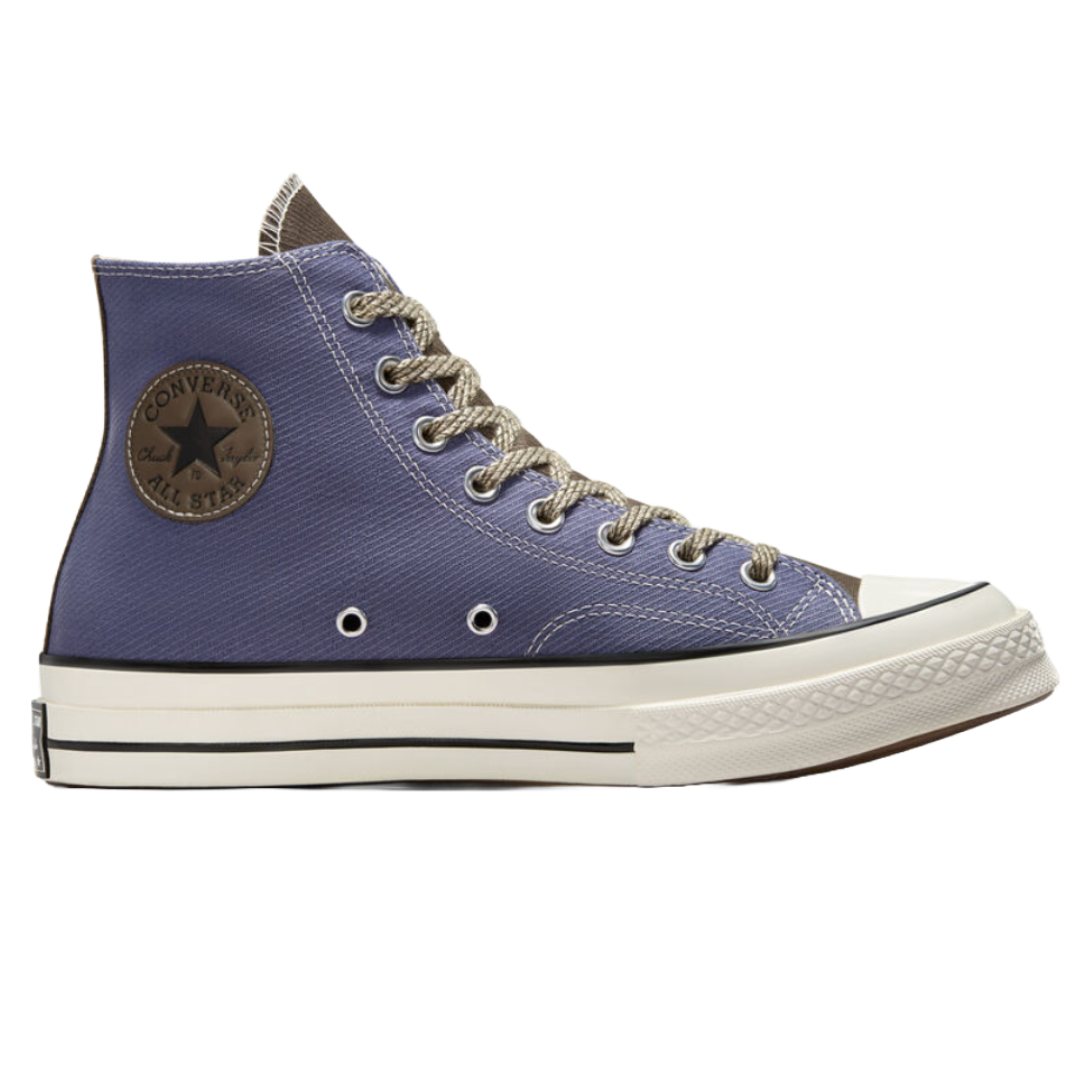Converse Men's Chuck 70 Shoes feature a high-top design in a bluish color with a brown patch, complemented by gray laces and a white rubber sole with black accents.