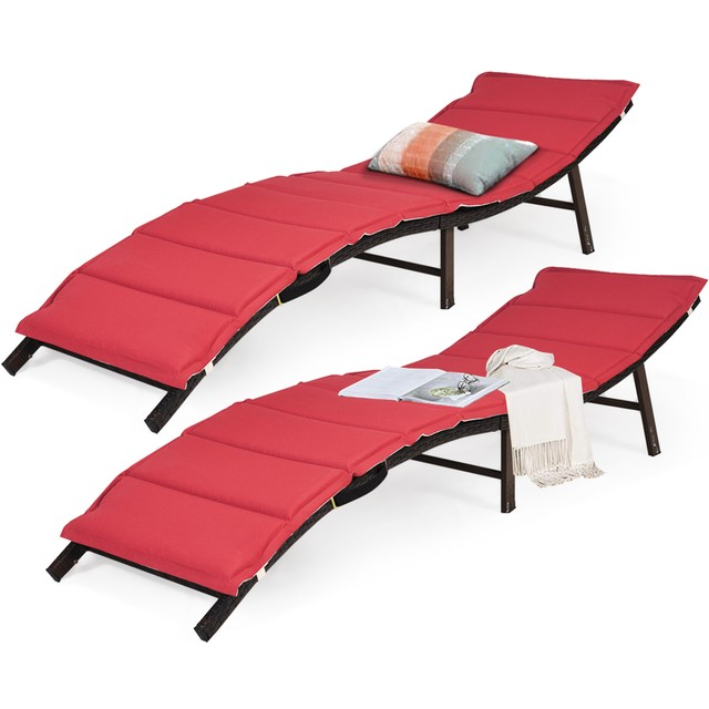 Two stackable folding lounge chairs with curved designs and red cushioned surfaces. They feature sturdy frames and include a multi-colored pillow and a blanket for added comfort.