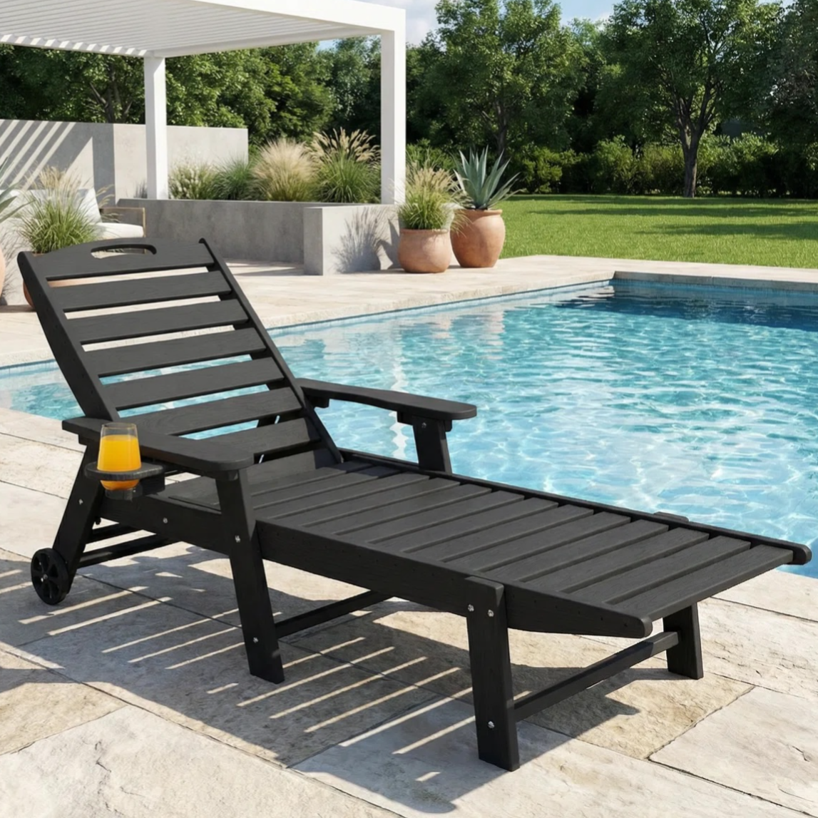 A black outdoor chaise lounge with wheels and a side cup holder is positioned by a pool, surrounded by a green lawn and potted plants, under a white pergola.