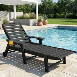 A black outdoor chaise lounge with wheels and a side cup holder is positioned by a pool, surrounded by a green lawn and potted plants, under a white pergola.