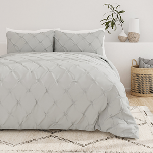 A neatly made bed with a gray tufted comforter set paired with matching pillows, placed in a room with decorative items.