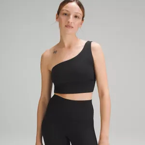 A person is wearing a black one-shoulder sports bra top and high-waisted leggings.