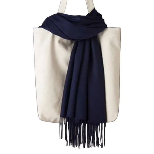 A cream-colored tote bag with two handles is adorned with a navy blue scarf featuring fringe detail.