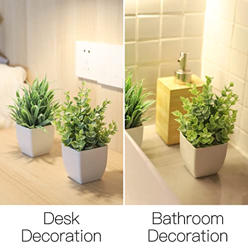 Two small artificial green plants in white square pots used as desk and bathroom decorations.