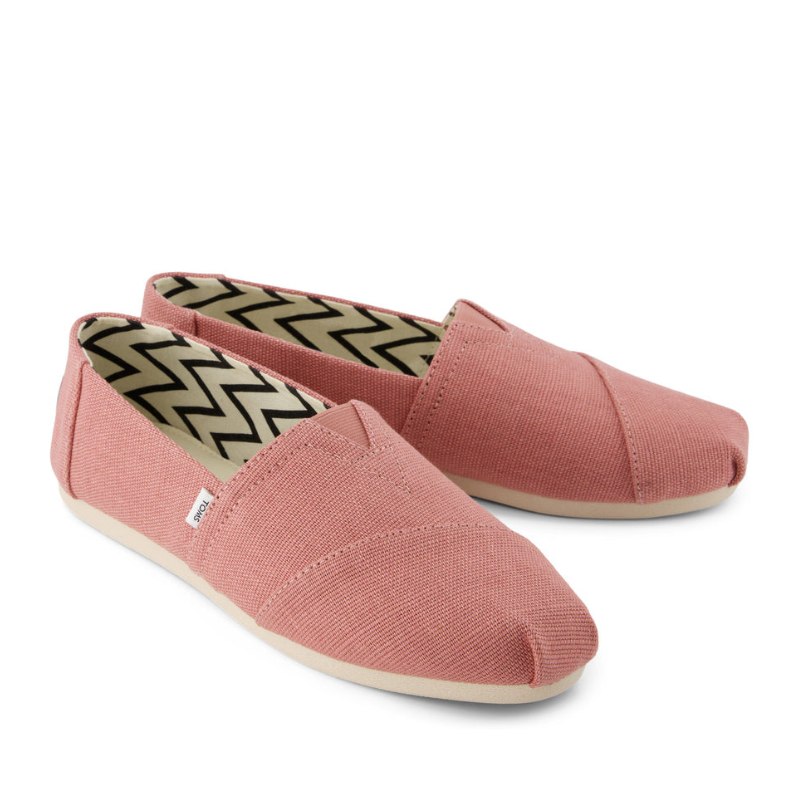 Pink slip-on shoes with a textured fabric upper and beige soles, featuring a black and white chevron pattern inside.