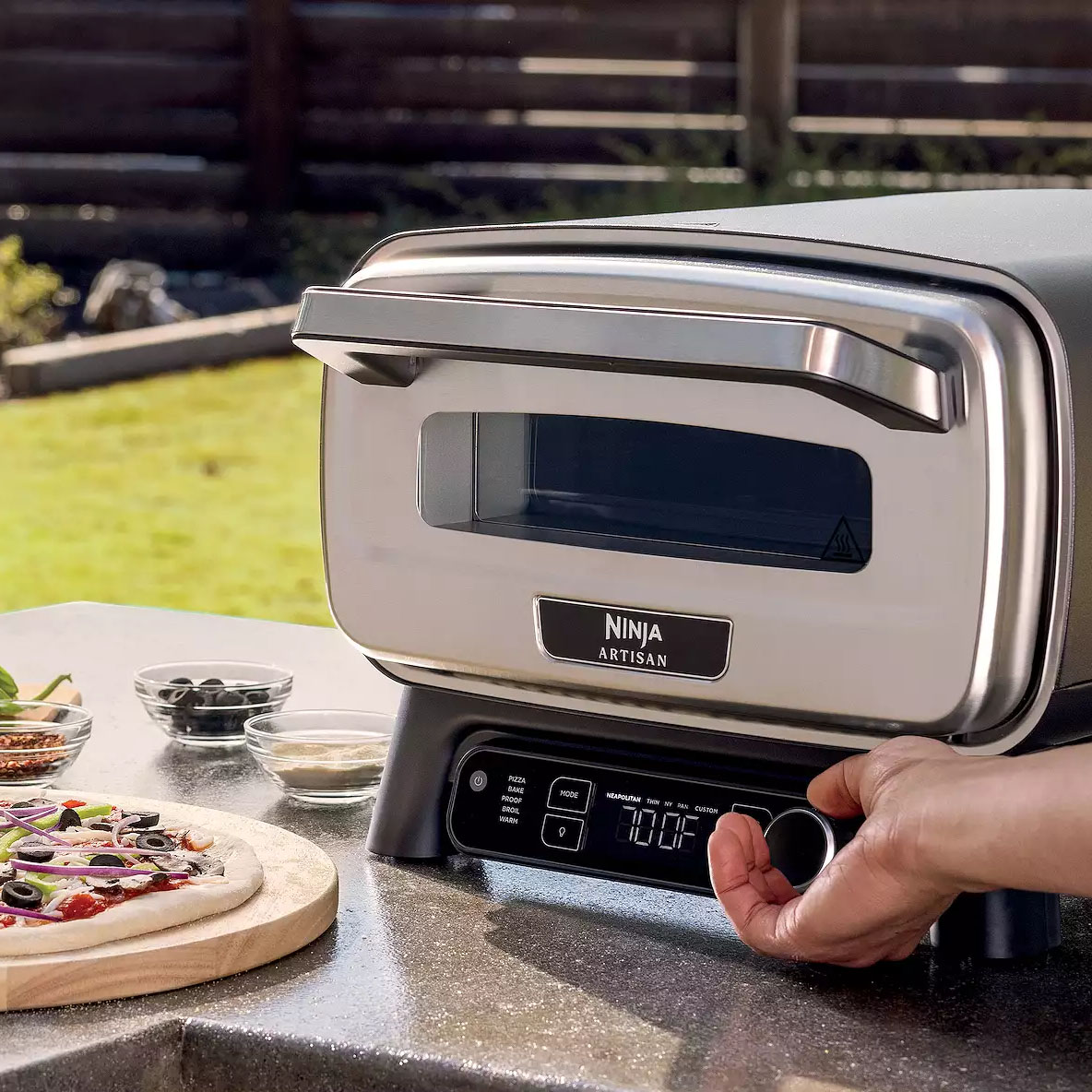 The Ninja Artisan Pizza Oven is a compact outdoor oven with a sleek stainless steel design, featuring a digital temperature display and control knob, ideal for baking pizzas.