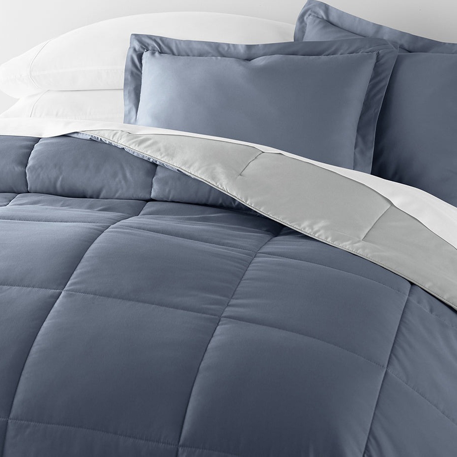 A bed with a blue comforter and matching pillowcases, accompanied by white pillows and a gray blanket edge.